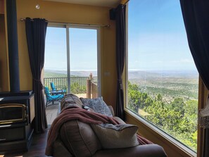 A room with a sofa, a fireplace, and a view of a mountainous landscape through a large window.