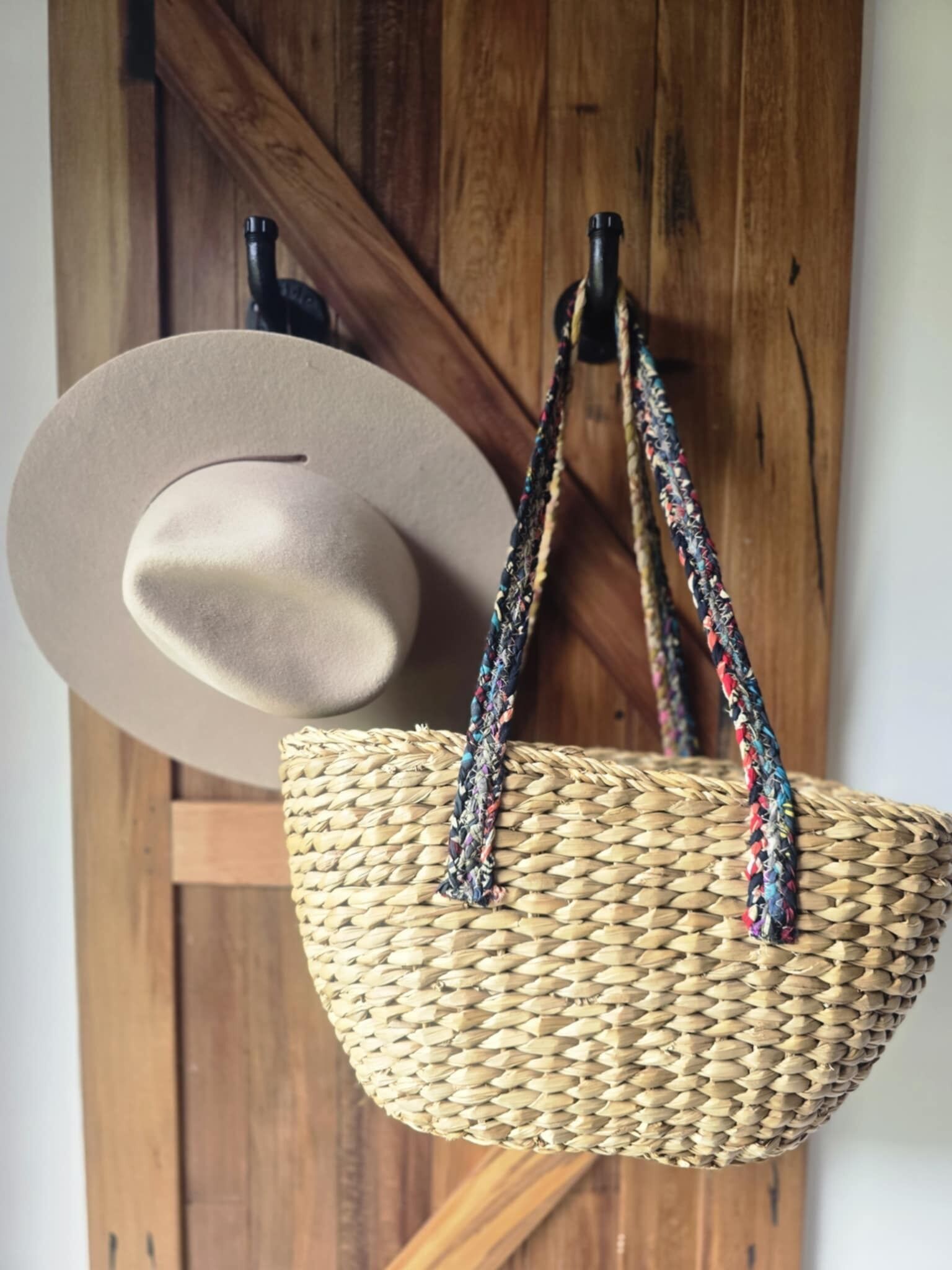 Un cesto intrecciato con un manico e un cappello appesi a una porta di legno.