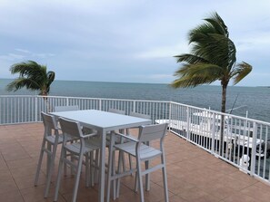 Eine Terrasse mit Tisch und Stühlen, einem weißen Geländer und Blick aufs Meer.