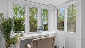 Ett rum med ett stort fönsterparti som vetter ut mot en trädgård, en krukväxt och en vas på fönsterbrädan.