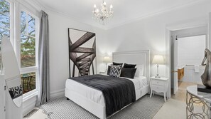 A bedroom with a large bed, bedside tables, a chandelier, and a view of the outdoors. - Grenville House - Beautiful Victorian home with garden in the heart of Daylesford (Daylesford)
