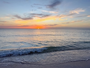 Un coucher de soleil sur une mer calme, où les vagues viennent doucement se briser sur le rivage.