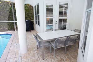 Um alpendre coberto com piscina, mesa e cadeiras, e churrasqueira.