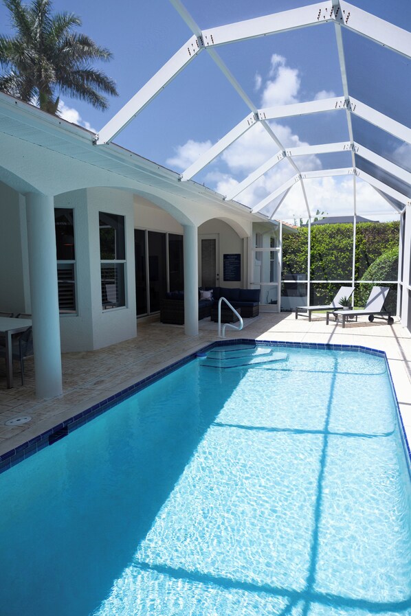 Uma área de piscina com piscina azul translúcida, espreguiçadeiras e um espaço de estar coberto.