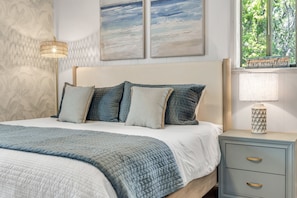 A bedroom with a bed, pillows, a bedside table, a lamp, and artwork on the wall. - Bethune Beach 4BR Home with Rooftop Deck Walk to Beach and Indian River (New Smyrna Beach)