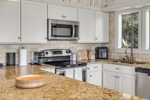 A modern kitchen with white cabinetry, a stainless steel microwave, a built-in oven, and a granite countertop. - Bethune Beach 4BR Home with Rooftop Deck Walk to Beach and Indian River (New Smyrna Beach)