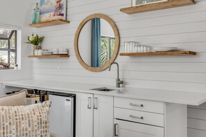 A modern kitchen with a central island, white cabinetry, and a large mirror above the sink. - Bethune Beach 4BR Home with Rooftop Deck Walk to Beach and Indian River (New Smyrna Beach)
