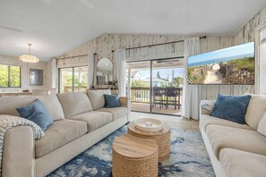 A spacious living room with a large sofa, a coffee table, and a television. - Bethune Beach 4BR Home with Rooftop Deck Walk to Beach and Indian River (New Smyrna Beach)