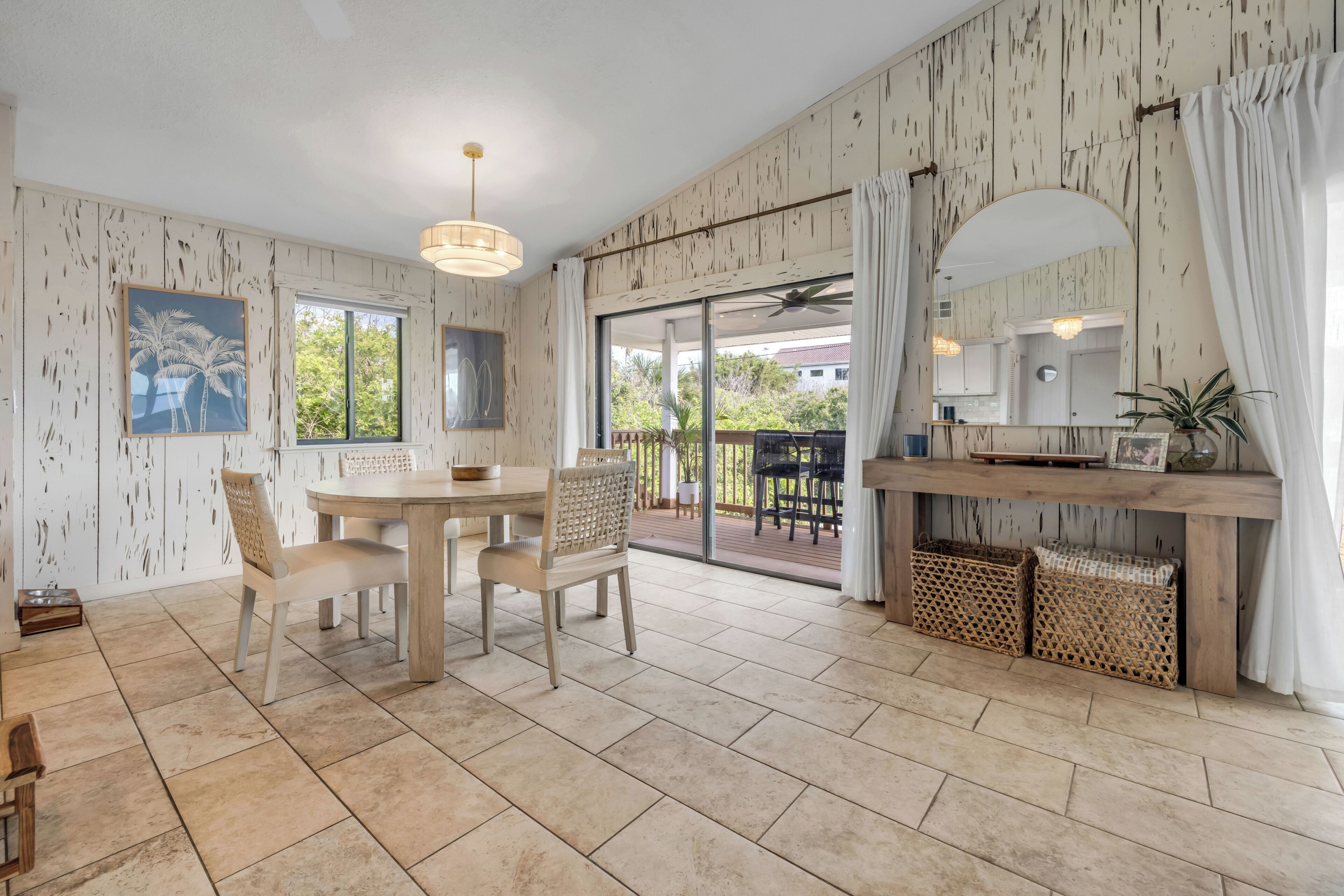 Une pièce spacieuse comprenant un coin repas, une grande porte-fenêtre coulissante donnant sur une terrasse extérieure et un coin cuisine avec vue sur l’extérieur.