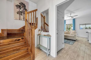 A modern interior with a wooden staircase, a living area with a sofa, and a dining space with a table and chairs. - Bethune Beach 4BR Home with Rooftop Deck Walk to Beach and Indian River (New Smyrna Beach)