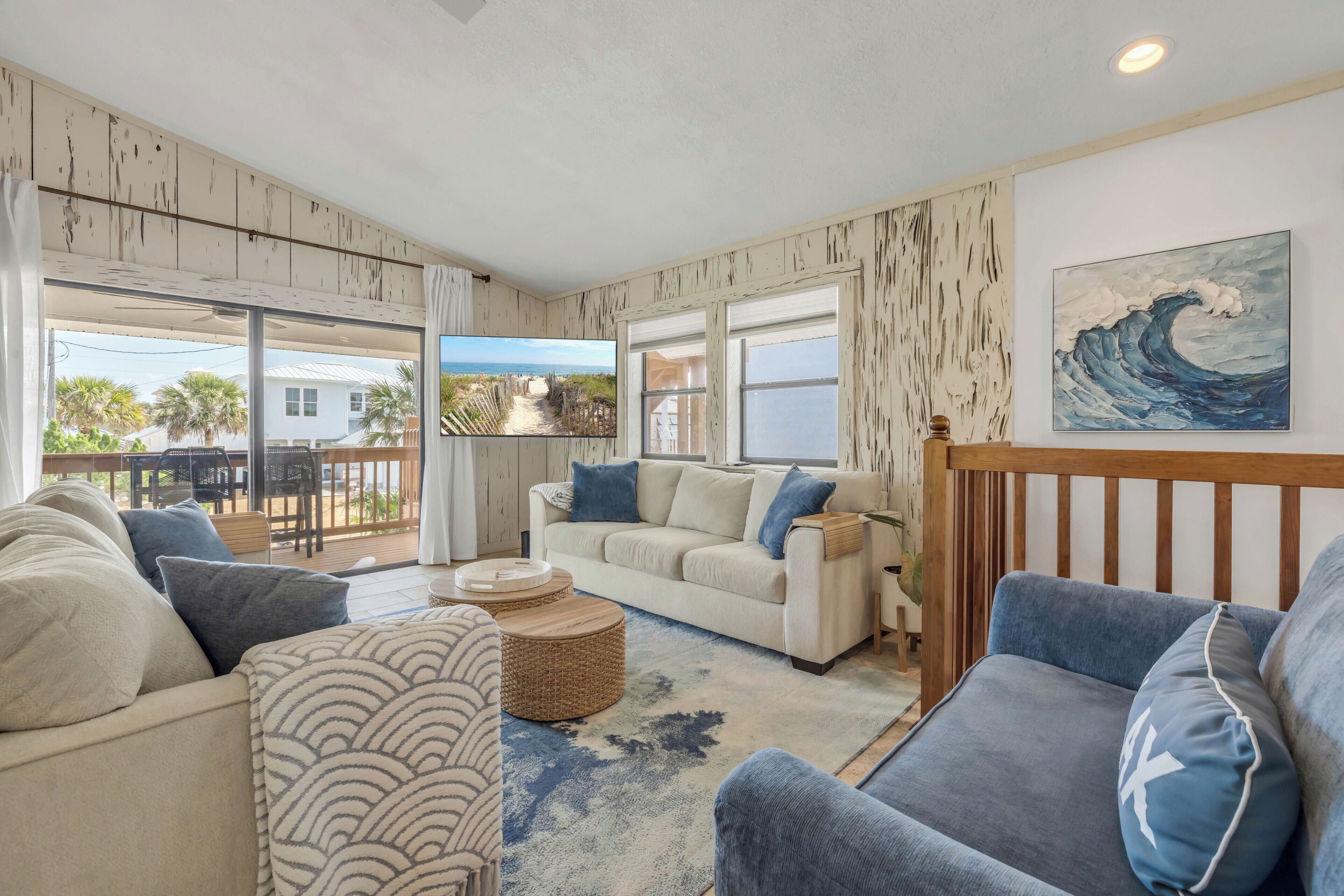 Una sala de estar con vista a la playa, un sofá blanco, un sillón azul y un cuadro de una ola.