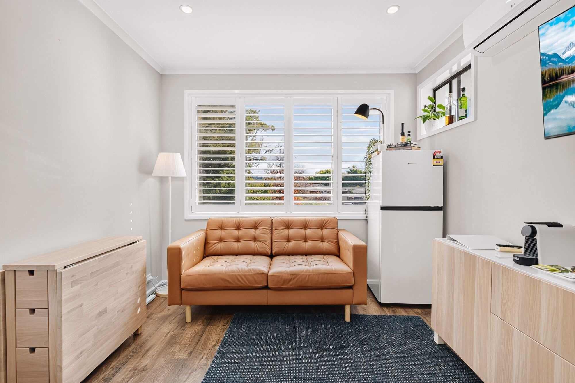 Cocina compacta con sofá, refrigerador, lámpara y ventana con persianas.