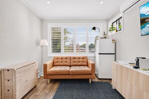 Eine kompakte Küche mit einer Couch, einem Kühlschrank, einer Lampe und einem Fenster mit Jalousien.