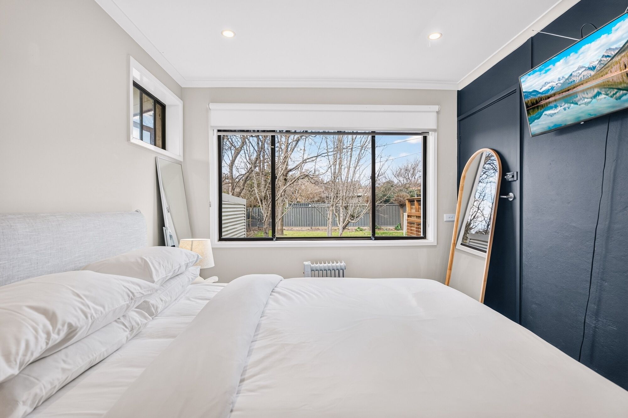 Een slaapkamer met een groot bed, een raam met uitzicht op bomen en een deur met een spiegel.