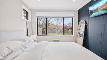 A bedroom with a large bed, a window with a view of trees, and a door with a mirror.