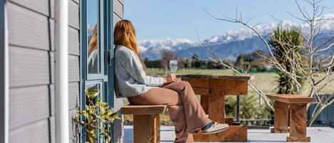A person sitting on a wooden bench outside a building with a view of mountains in the background.