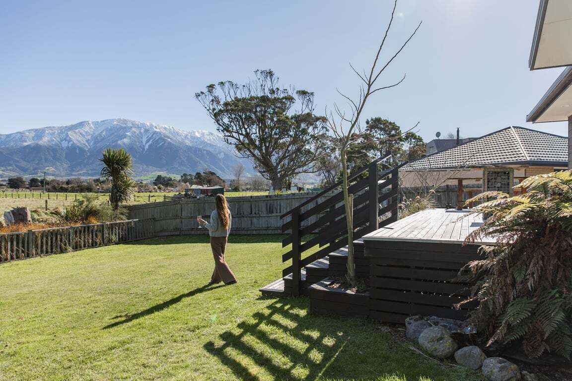 A grassy outdoor area with a wooden staircase leading to a covered deck, a mountain in the background, and a person walking.