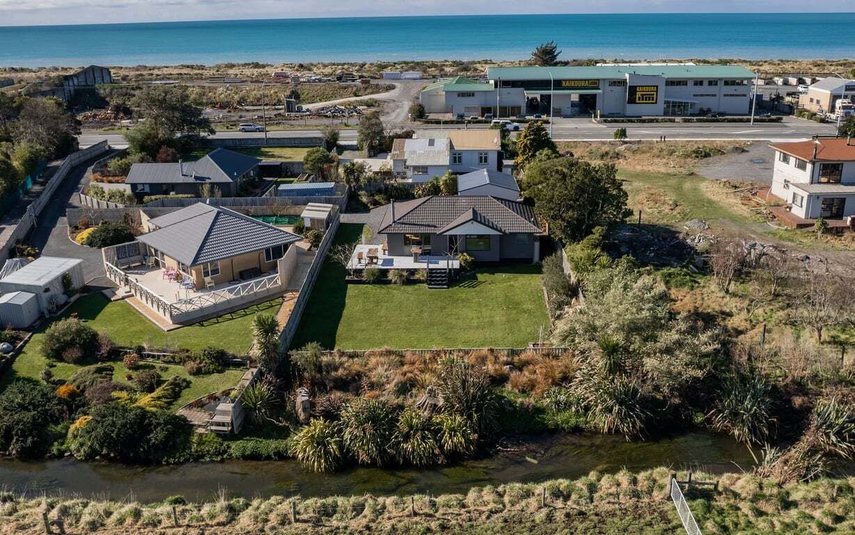 An aerial view of a coastal residential area with houses, a swimming pool, and a beach in the background.