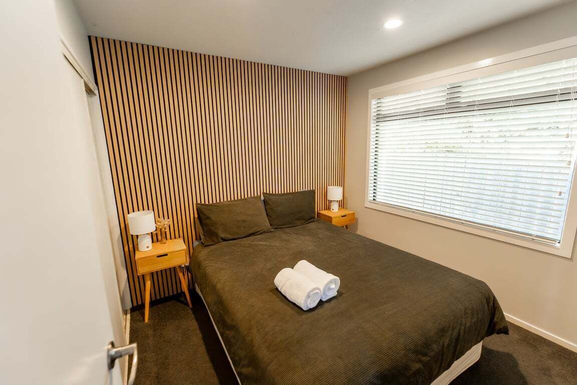 Een slaapkamer met een bed, twee nachtkastjes, een raam met zonwering en een gestreepte wand.
