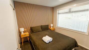 Een slaapkamer met een bed, twee nachtkastjes, een raam met zonwering en een gestreepte wand.