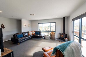 Een moderne woonkamer met een hoekbank, een open haard en grote ramen.