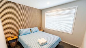Une chambre d’hôtel comprenant un lit, une table de chevet, une lampe, une fenêtre avec des stores et un mur avec des lambris verticaux.