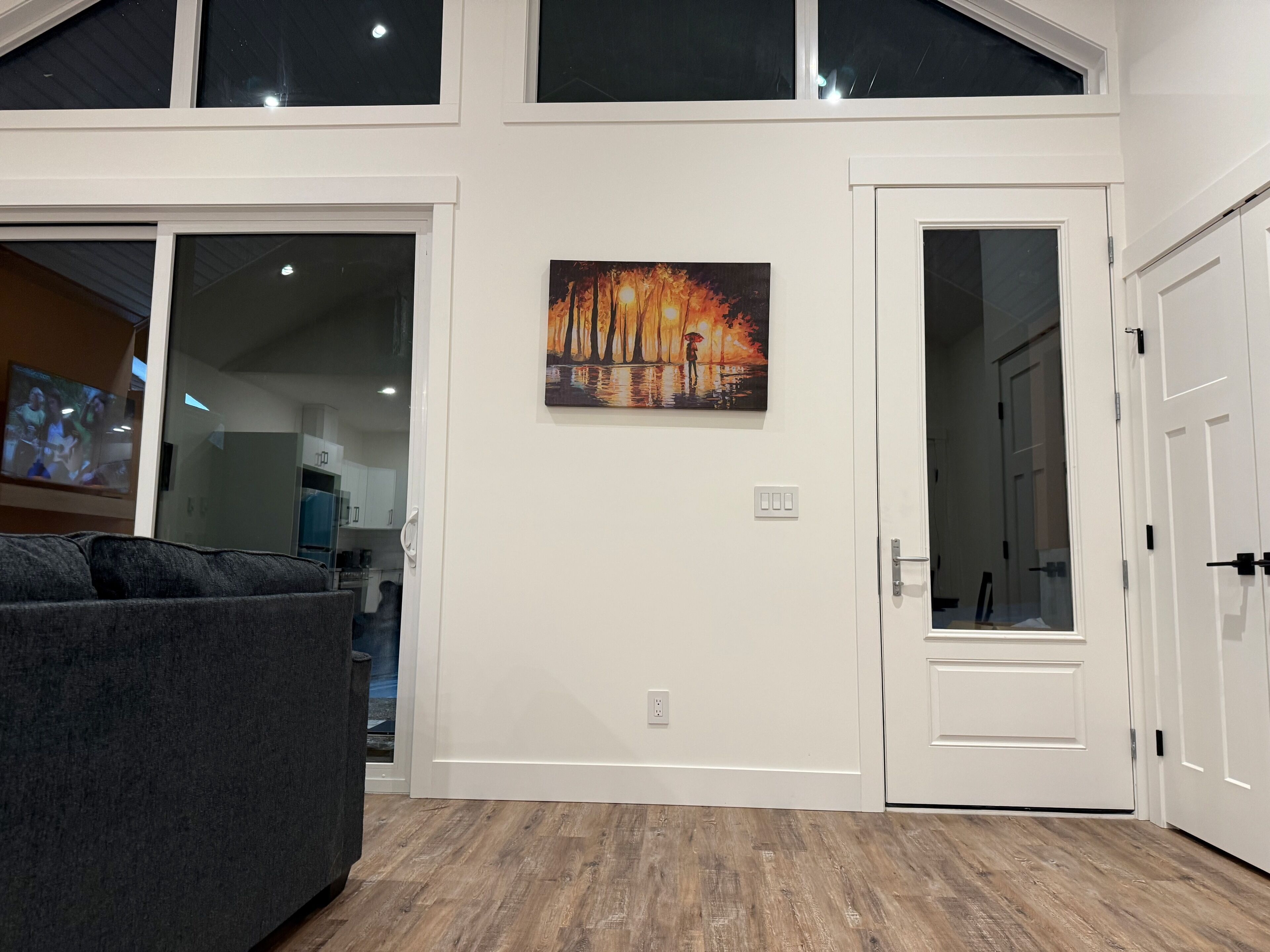 A modern interior with a large window, a painting of a sunset, and a door leading to a room.