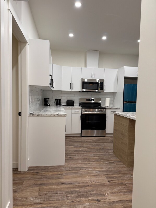 A modern kitchen with white cabinetry, a microwave, a coffee maker, and a refrigerator.