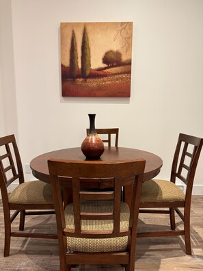 A dining table with a vase centerpiece, surrounded by wooden chairs with woven seats, against a plain wall.