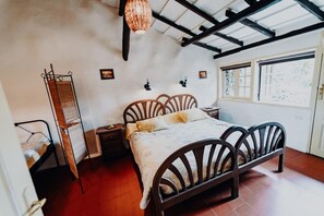Un dormitorio con una cama de madera, una mesita de noche, una lámpara colgante, una ventana con persianas y una estantería en la pared.