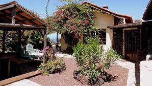 A rustic building with a stone facade, a wooden pergola, and a garden with various plants and flowers.