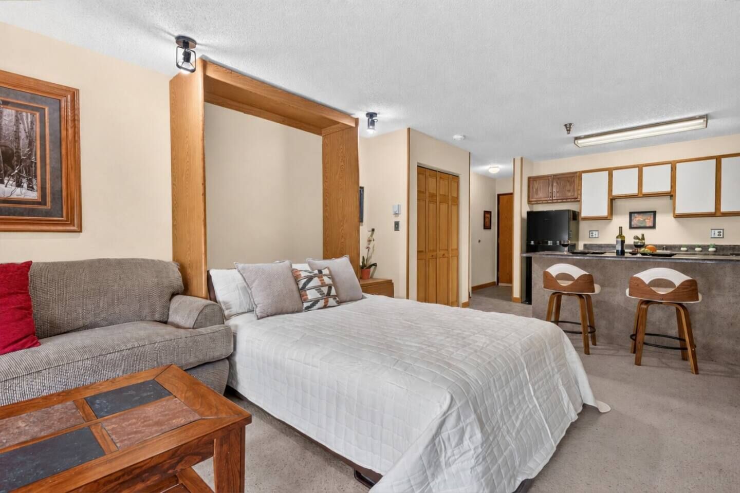 Ein Schlafzimmer mit Bett, einer Couch, einem kleinen Tisch und einer Küchenzeile mit einer Theke und Hockern.