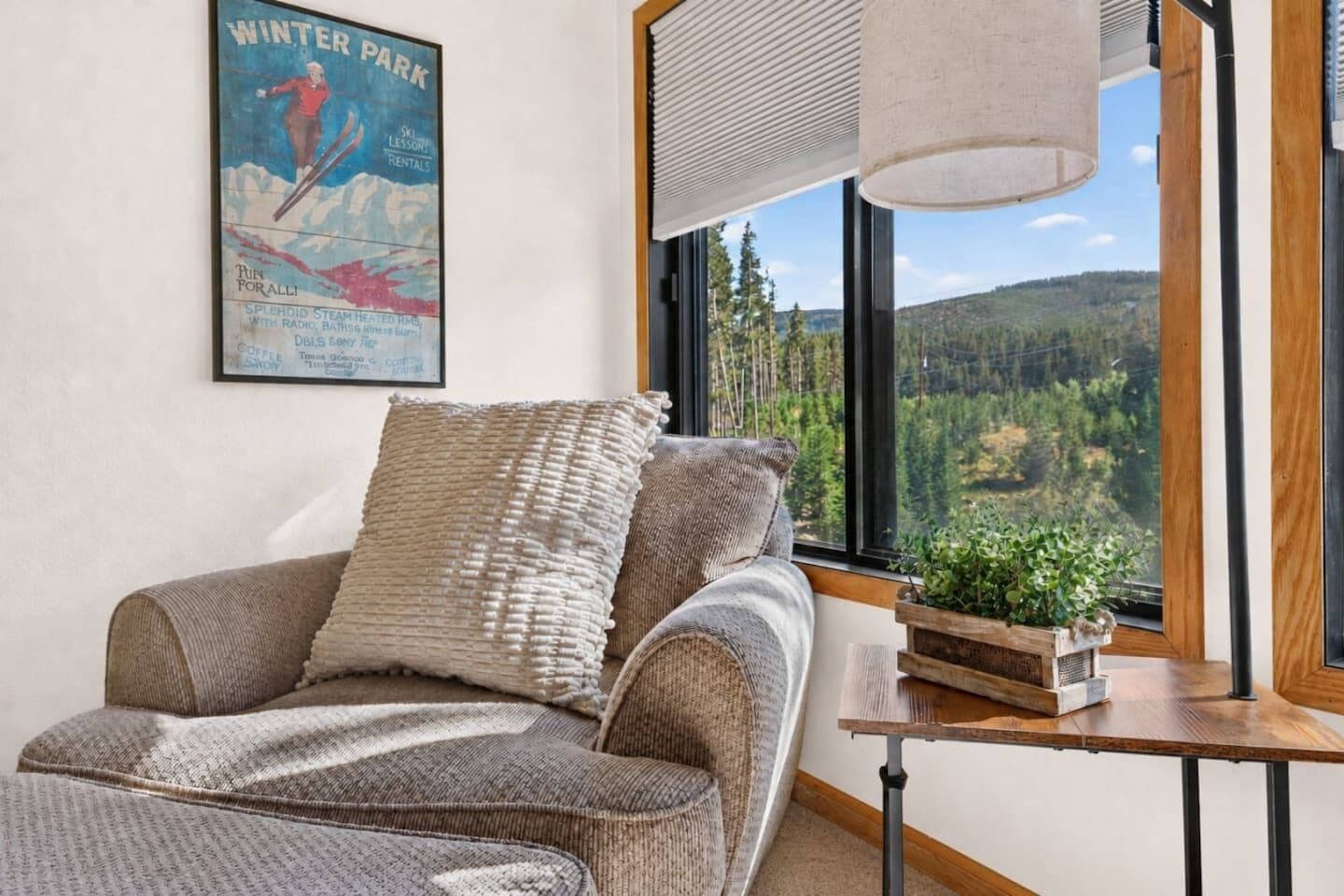 Ein gemütliches Zimmer mit großem Fenster und Blick auf eine bewaldete Landschaft, ein bequemer Sessel mit strukturierter Sitzkissen sowie ein alter Kunstdruck an der Wand.
