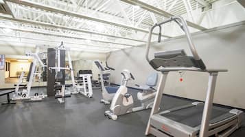 Een fitnessruimte met diverse trainingsapparaten, waaronder loopbanden, krachttrainingsmachines en een roeimachine.