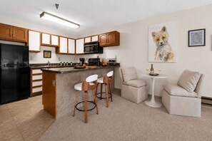 Eine moderne Küche mit einem schwarzen Kühlschrank, Holzschränken, einer Mikrowelle und einer Bar mit zwei weißen Barhocker.