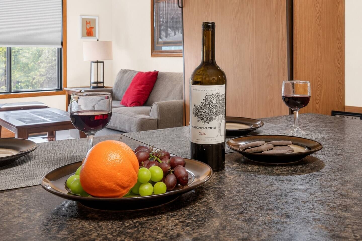 Et spisebord med en vinflaske, et glas rødvin og frugt anrettet på tallerkener.