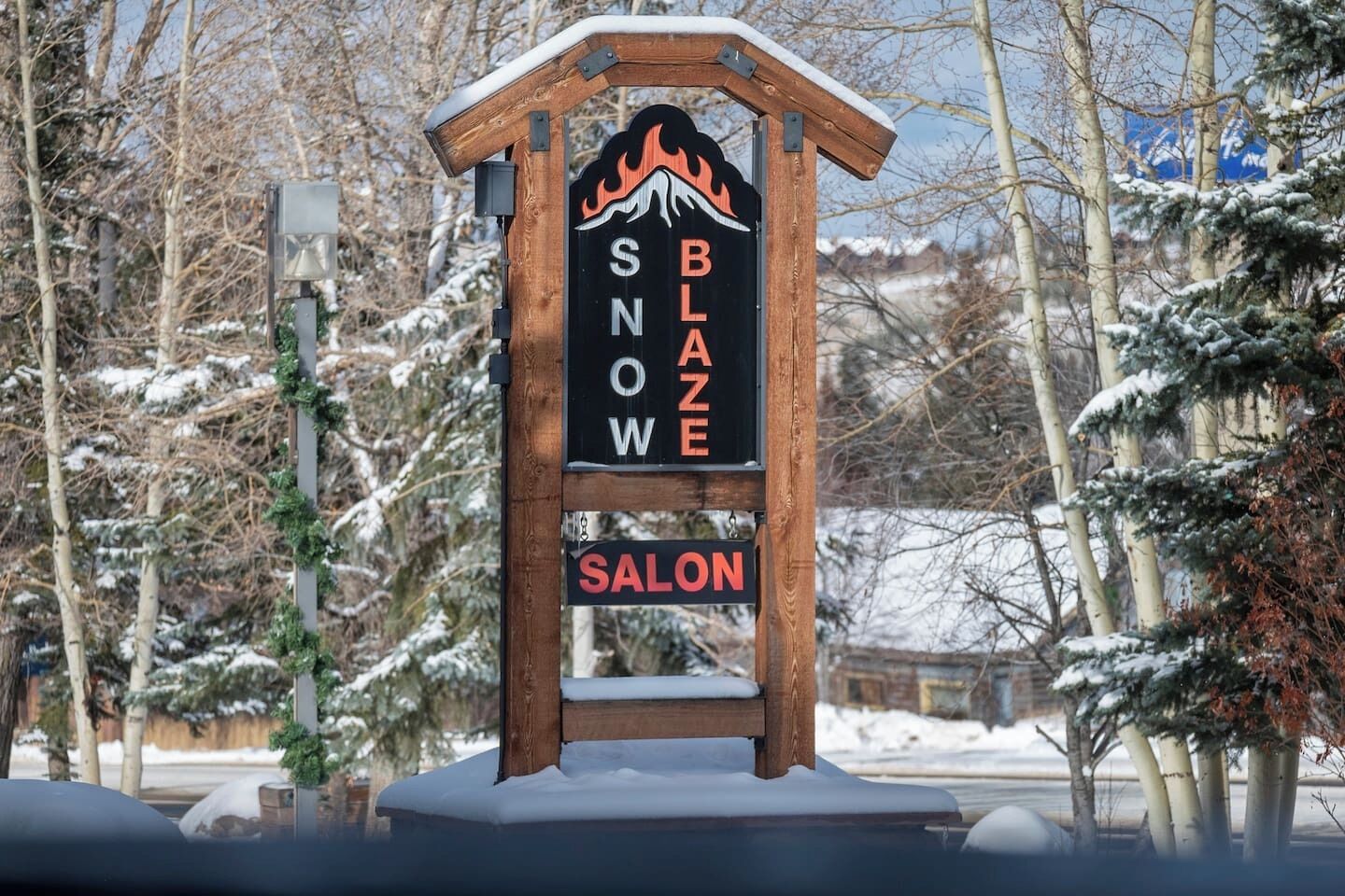 Un panneau en bois sur lequel sont inscrits les mots « SNOW BLAZE » et « SALON », entouré d’arbres couverts de neige.