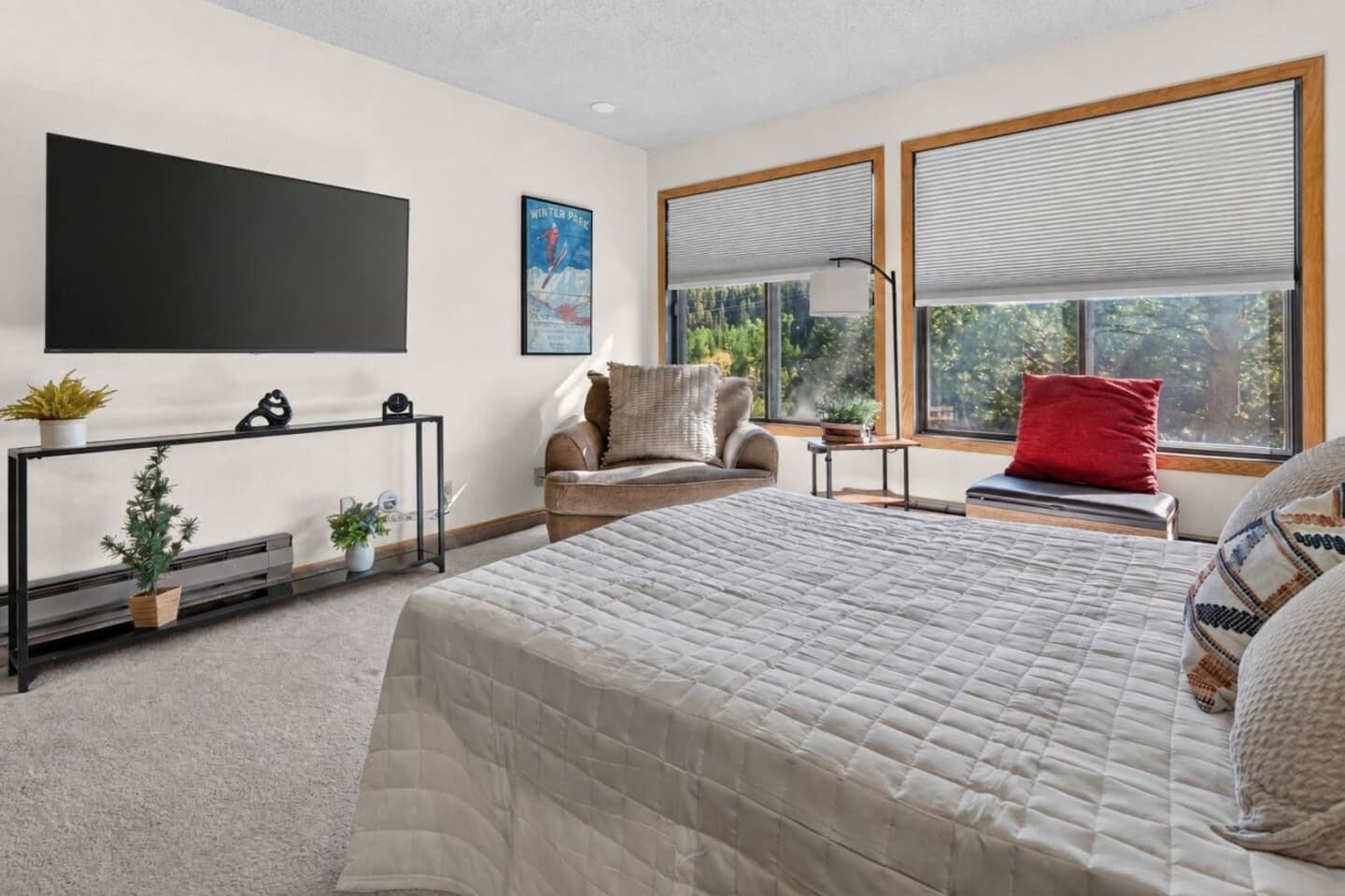 Ein modernes Schlafzimmer mit einem großen Bett, einer Couch, einem Fernseher und einem Fenster mit Jalousien.