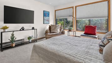 Een moderne slaapkamer met een groot bed, een bank, een televisie en een raam met jaloezieën.