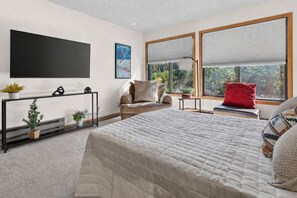 Ein modernes Schlafzimmer mit einem großen Bett, einer Couch, einem Fernseher und einem Fenster mit Jalousien.