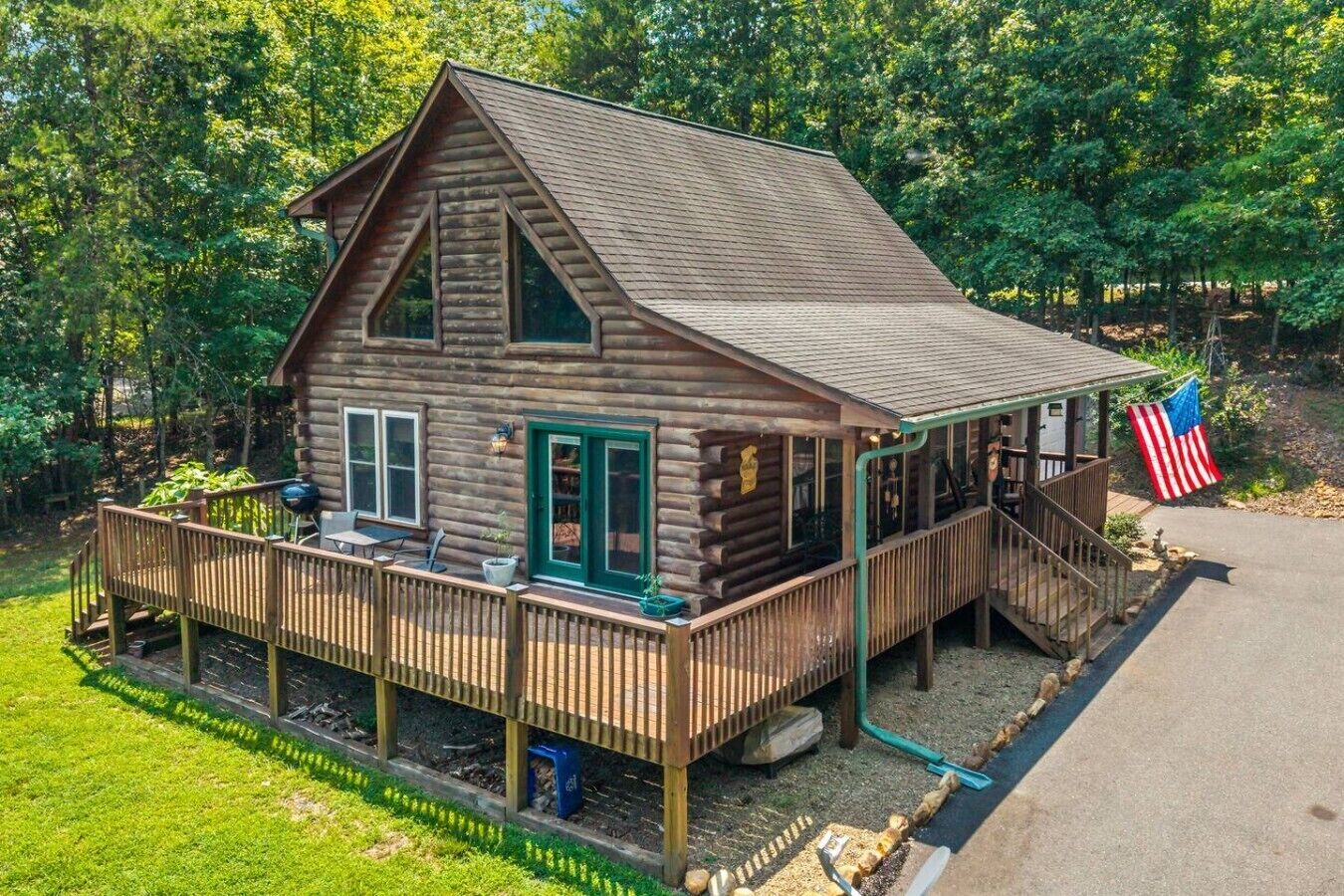 Une cabane en rondins avec une véranda, une terrasse et un drapeau américain.