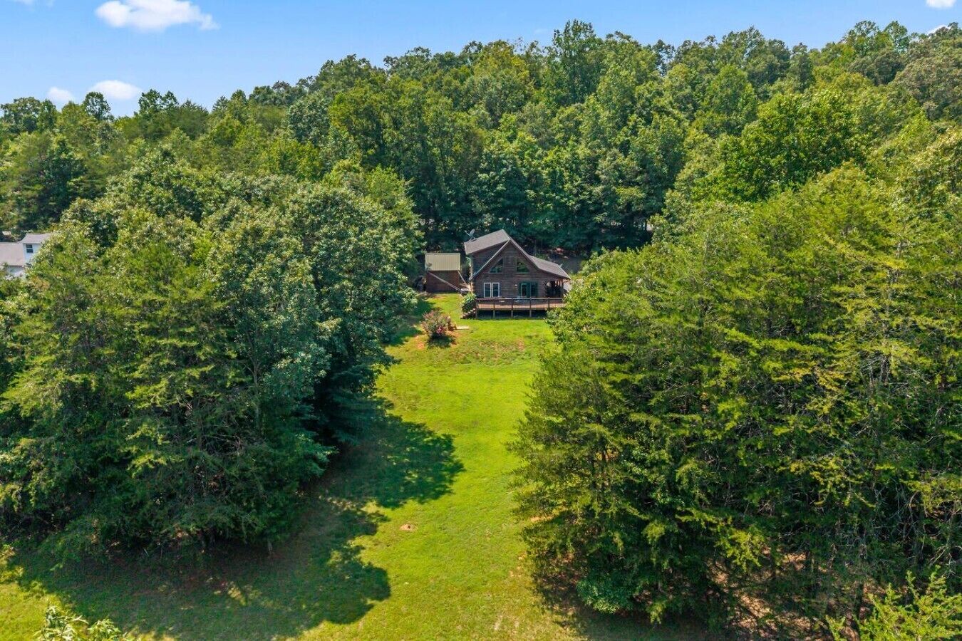 Une maison entourée d’une forêt dense, avec un chemin dégagé menant à l’entrée.