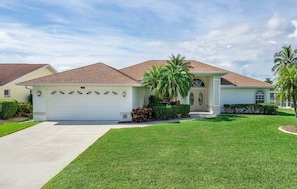 A single-story house with a white garage door, a front porch, and a well-maintained lawn. - Baju | Gulf Access | Pool & Spa |  Game Room (Cape Coral)