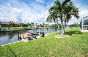 A waterfront property with a dock, a grassy area, and a palm tree. - Baju | Gulf Access | Pool & Spa |  Game Room (Cape Coral)