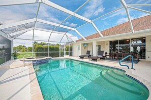 A covered swimming pool with lounge chairs and a patio area. - Baju | Gulf Access | Pool & Spa |  Game Room (Cape Coral)