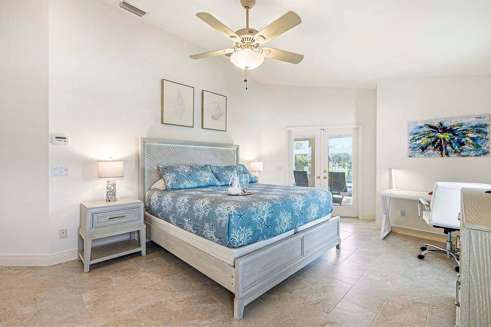 A bedroom with a bed, bedside tables, a ceiling fan, and a door leading to a balcony.