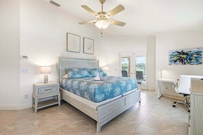 A bedroom with a bed, bedside tables, a ceiling fan, and a door leading to a balcony. - Baju | Gulf Access | Pool & Spa |  Game Room (Cape Coral)