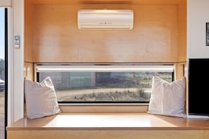 A room with a large window, a ceiling-mounted air conditioner, and a bench with pillows.