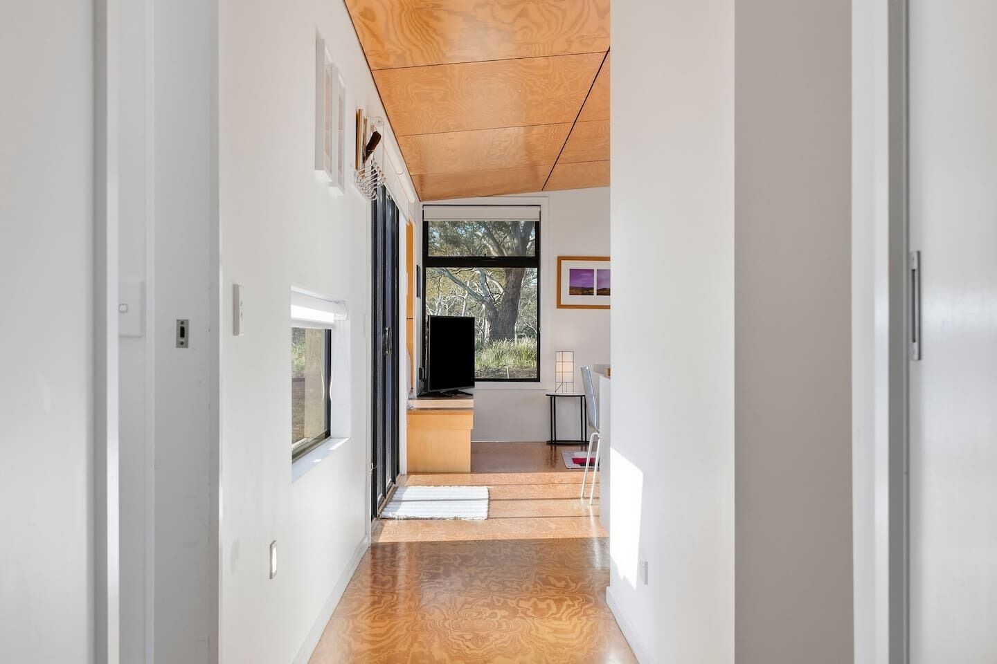Un couloir avec un plafond en bois, un téléviseur posé sur un meuble, et une vue sur l’extérieur par une fenêtre.