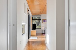 A hallway with a wooden ceiling, a television on a stand, and a view of the outdoors through a window.